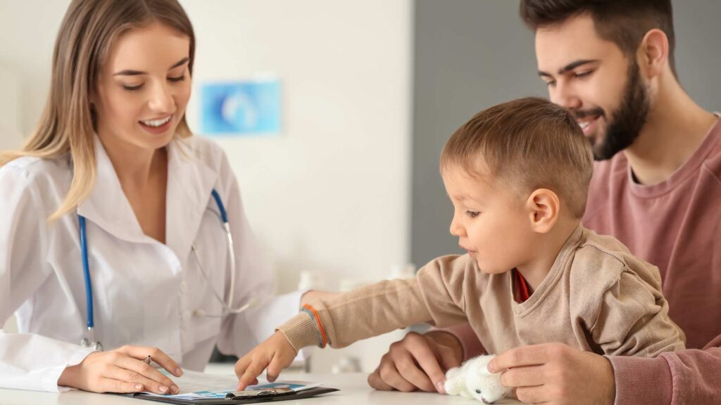 A doctor, a child, and an adult looking at a page together during a visit discussing why autism cure is a misconception