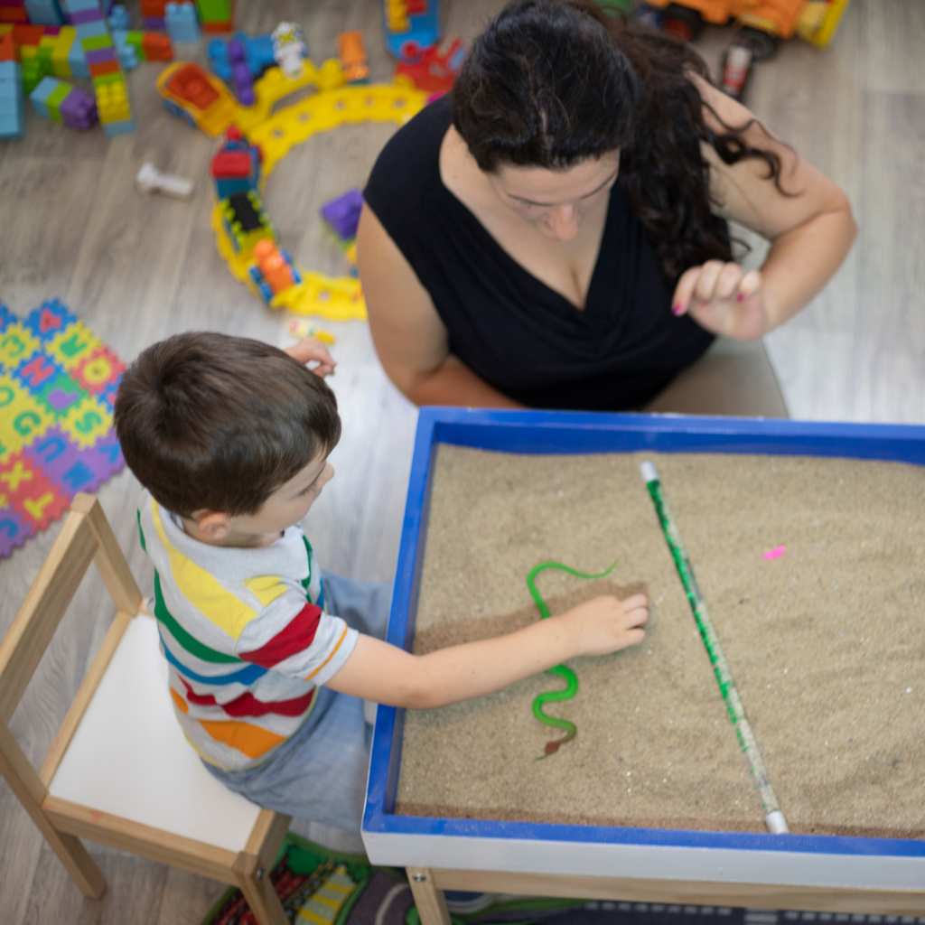 Adult and child working together with a sand tray during a home ABA learning activity.
