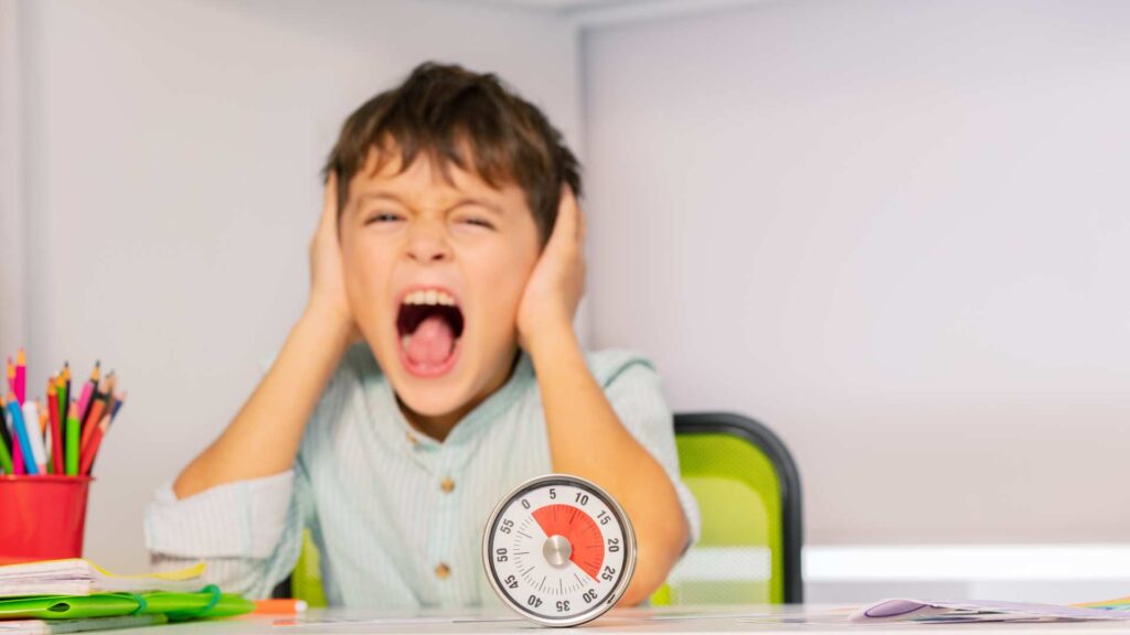 Child covering ears and yelling at a desk with a timer, showing challenging behaviors in autism.