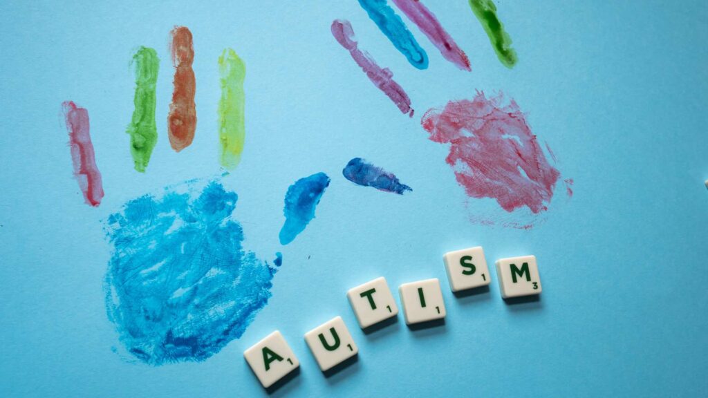 Colorful painted handprints on a light blue background with small letter blocks spelling autism