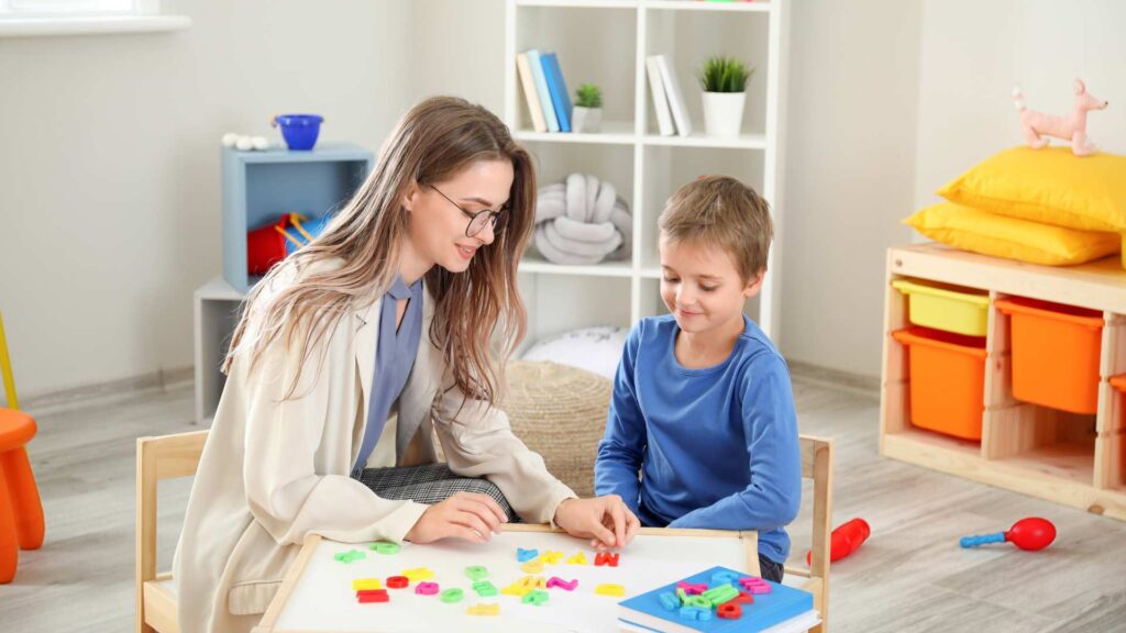 Child placing bright pieces on a board while an adult supports them during autism play-based therapy.