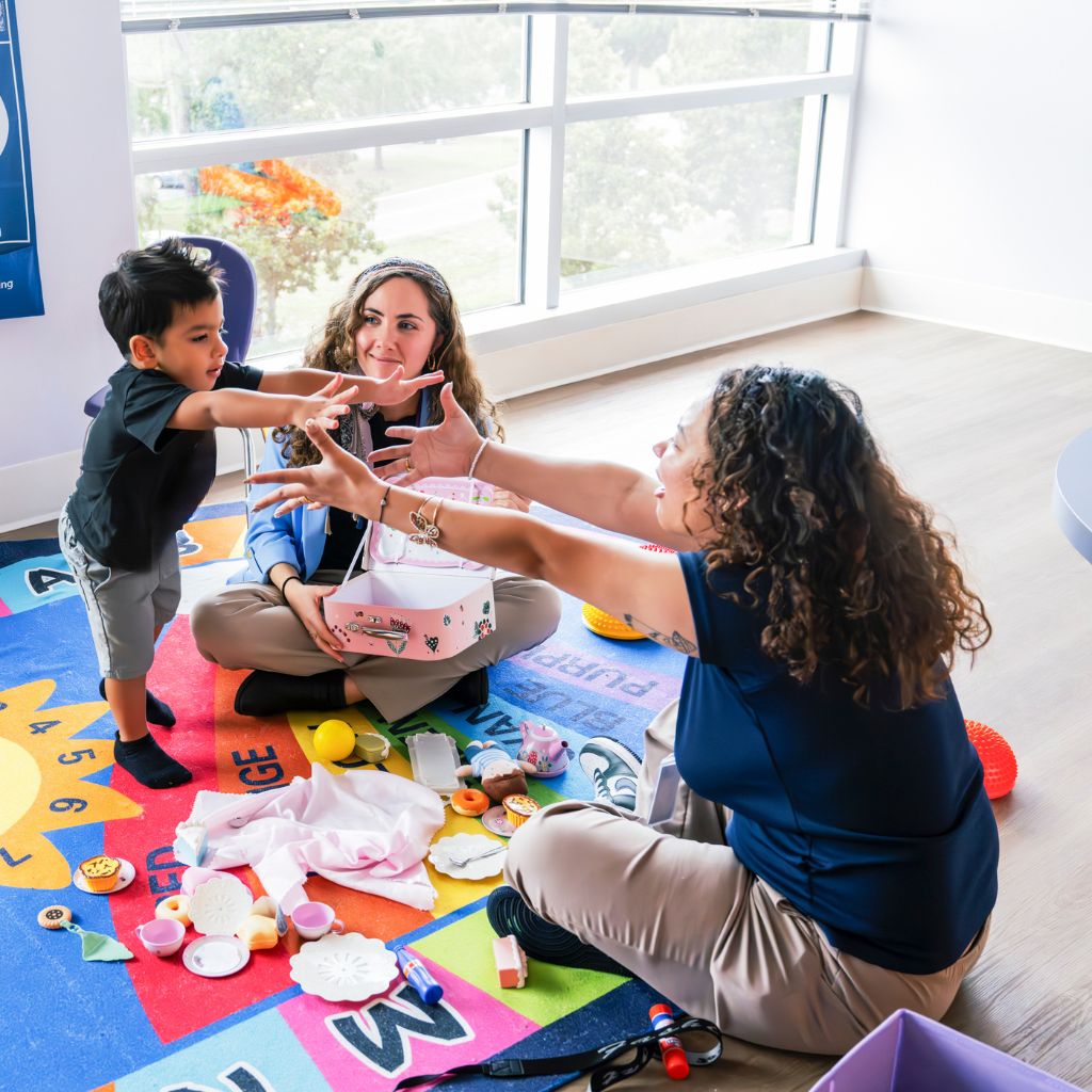 ABA therapists engaging a young boy in a play-based therapy session on a colorful mat