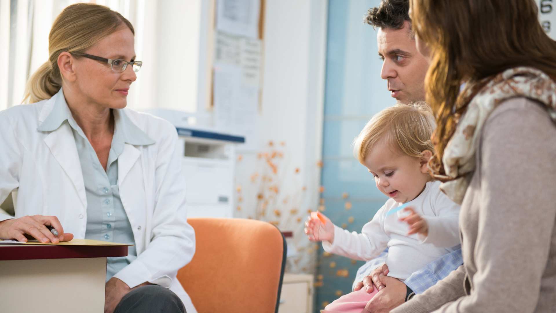 Parents hold their toddler while discussing autism concerns with a pediatrician in a clinic office